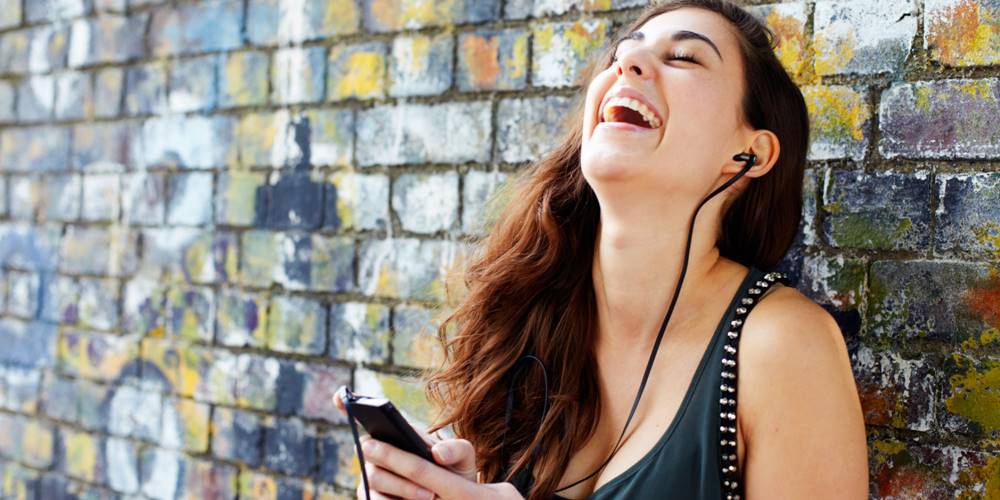 Young woman laughing with smart phone + headphones
