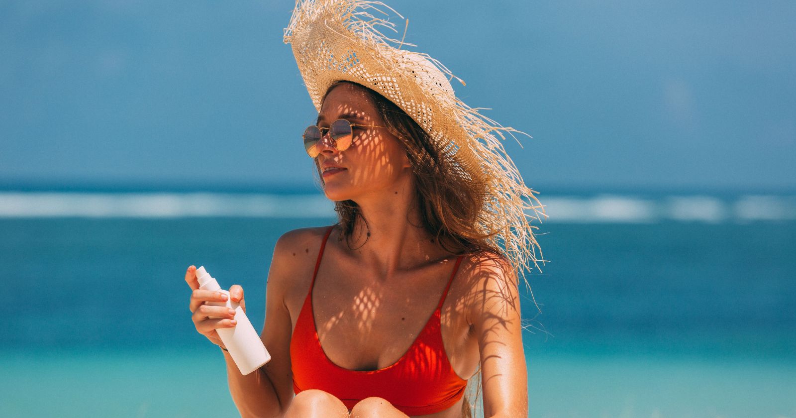 žena na pláži s SPF v ruke