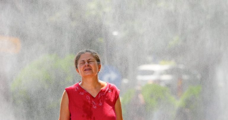 Žena kráča cez vodná hmlu, ktorú nainštalovala miestna samospráva počas horúčav