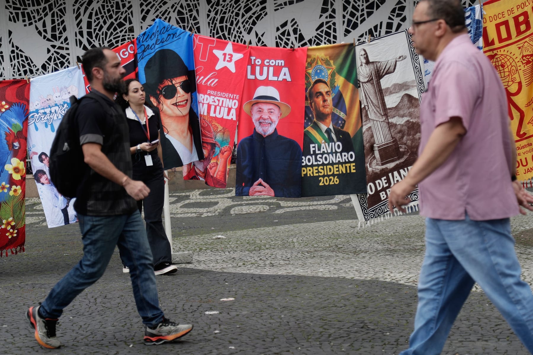 Ľudia v Riu de Janeiro kráčajú okolo kampaňových vlajok Luiza Inacia Luly da Silvu a Flavia Bolsonara.